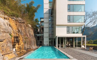 Un edificio moderno con piscina, zona de estar al aire libre y un acantilado rocoso.