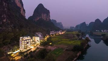 A riverside hotel with multiple floors, a swimming pool, and a view of the surrounding mountains.