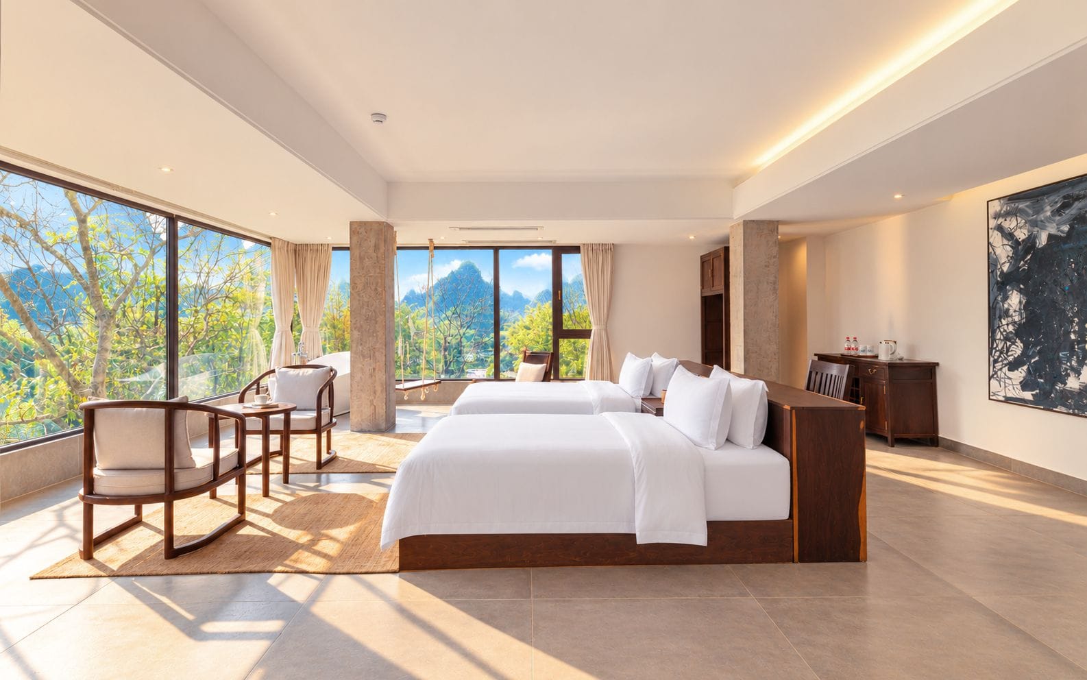 A modern hotel room with a large bed, a seating area, and a view of a mountainous landscape.