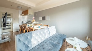 A modern living room with a large tufted sofa, a dining table set with chairs, and a kitchen area in the background. - Akitsu 703 Kyocera Dome 10 min walk Dotonbori Kansai Airport Osaka Castle Kaiyukan USJ 1 transfer Family friendly Free parking 15 (大阪府大阪市西区境川１丁目)