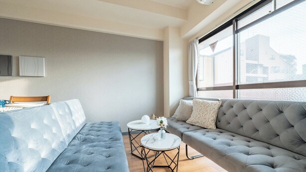 A modern living room with a grey sofa, a blue tufted sofa, and two round tables with white marble tops. - Akitsu 703 Kyocera Dome 10 min walk Dotonbori Kansai Airport Osaka Castle Kaiyukan USJ 1 transfer Family friendly Free parking 15 (大阪府大阪市西区境川１丁目)