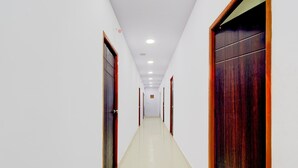 A long, narrow hallway with white walls and wooden doors on both sides. - Super Hotel O Kota Railway Junction (Kota)