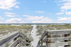 Une promenade en bois qui mène à une plage bordée de dunes, sous un ciel dégagé.