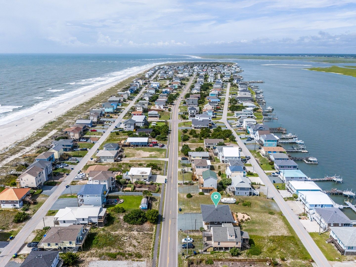 Una zona residencial costera con casas a lo largo de la playa y un puerto deportivo con barcos.