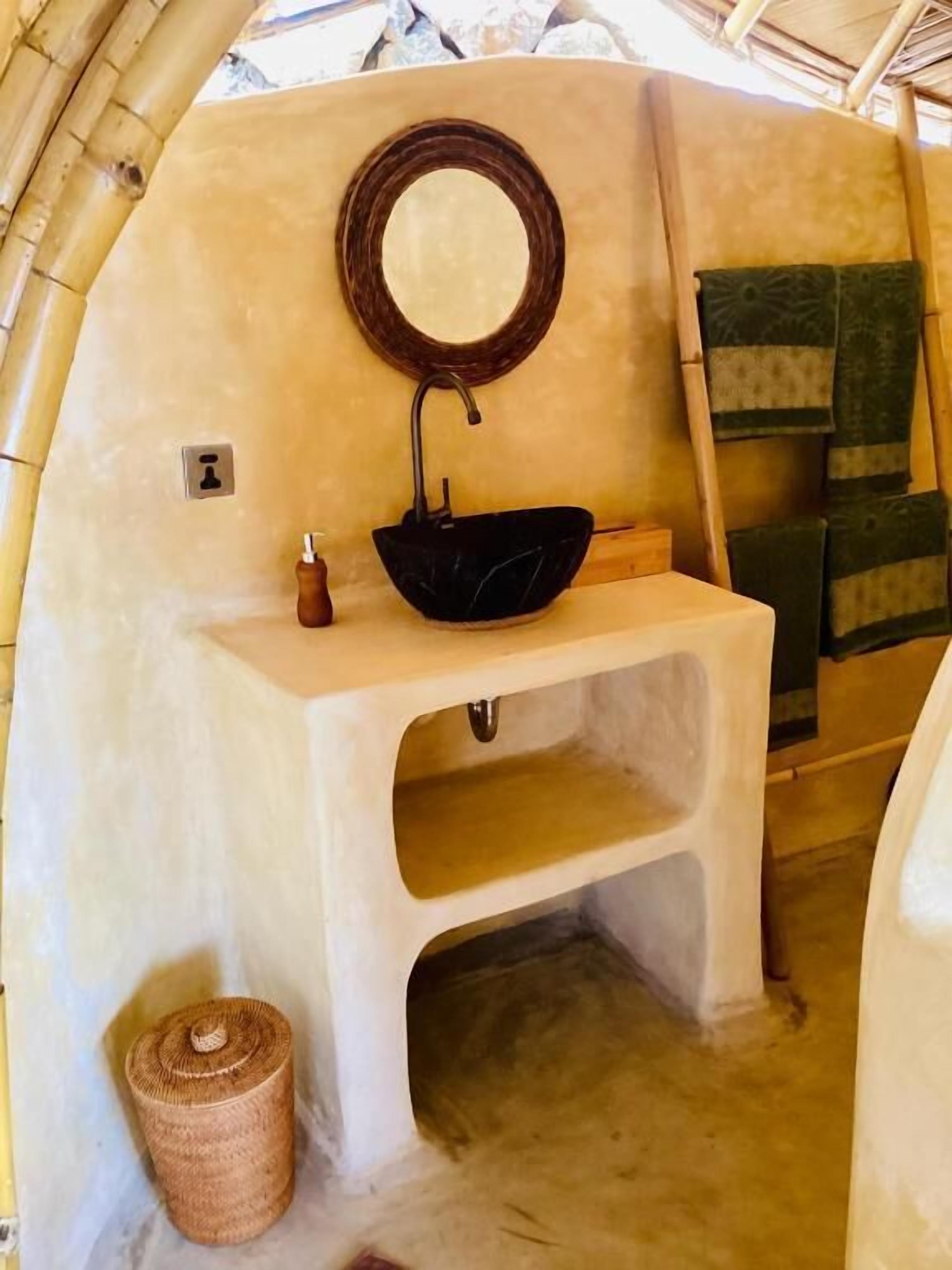 A bathroom with a black sink, a round mirror, and a wooden bench.