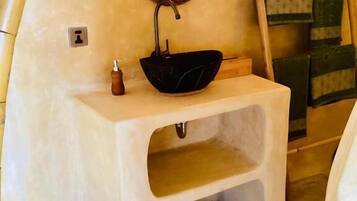 A bathroom with a black sink, a round mirror, and a wooden bench.