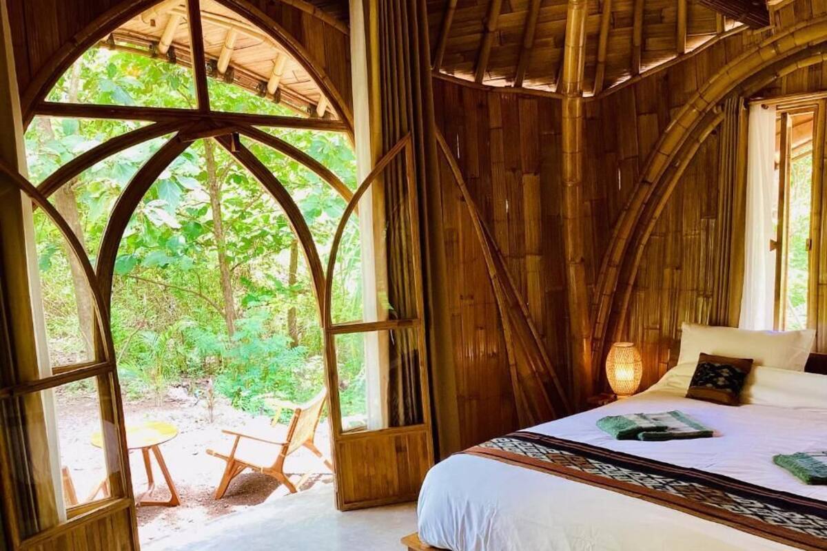 A rustic wooden room with a bed, a large window, and a small table with chairs.