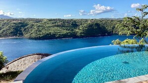 A infinity pool with a wooden deck and a view of a lake and forested hills.