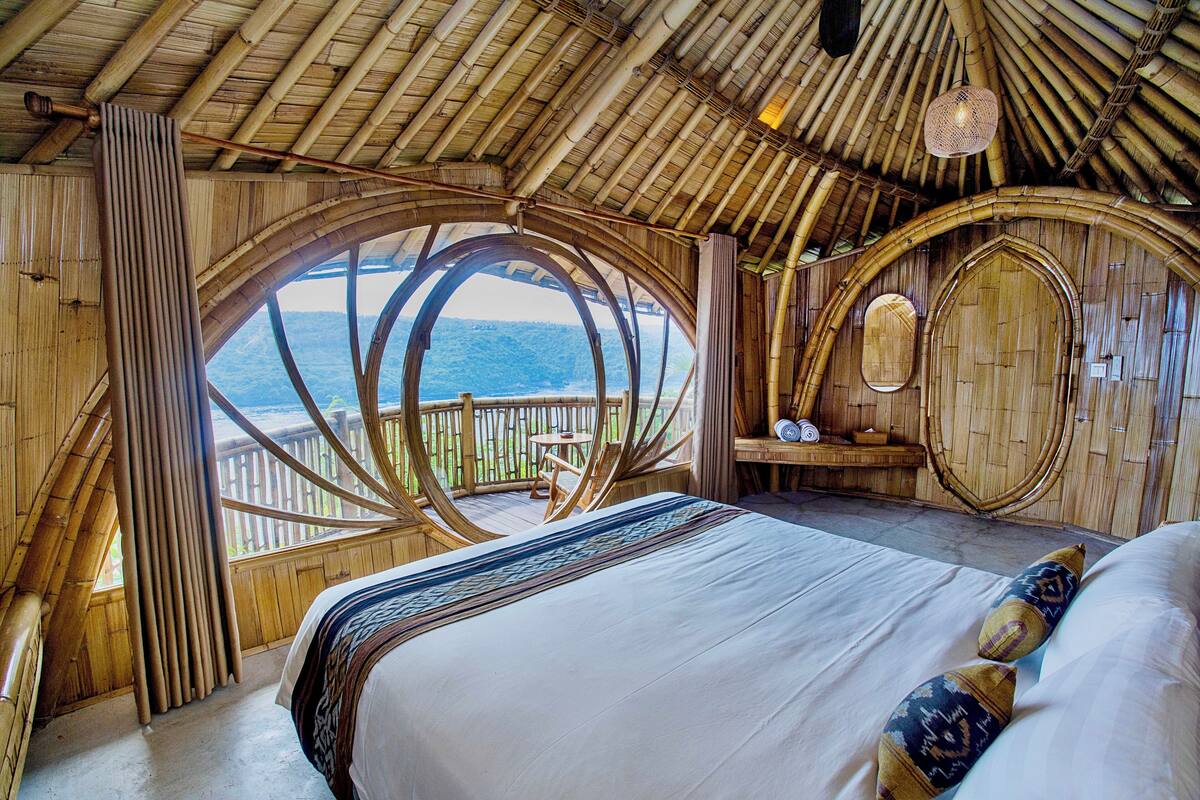 A room with a large bed, a wooden ceiling, and a view of the ocean.