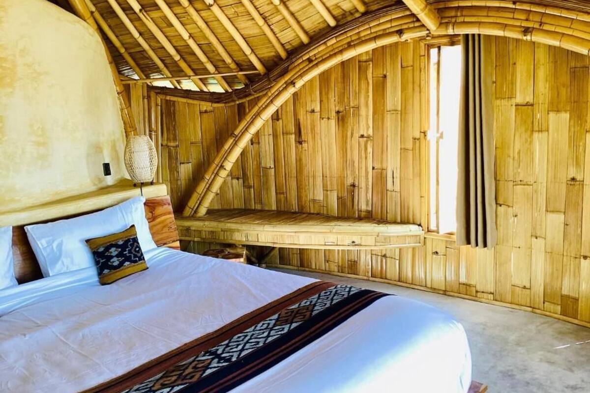 A room with a bed, a bench, and a curved wooden ceiling.