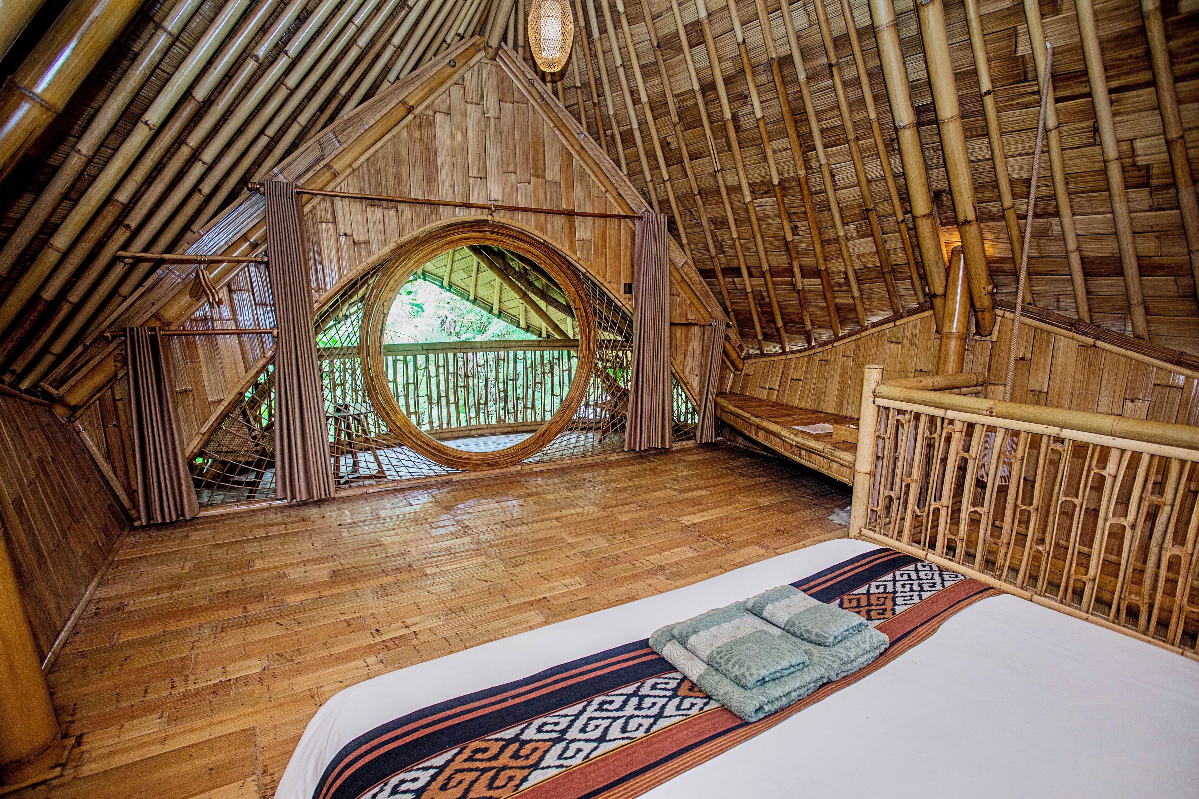 Une pièce dotée d’un plafond en pente en bois, d’une grande fenêtre circulaire et d’un lit surmonté d’un tapis à motifs.