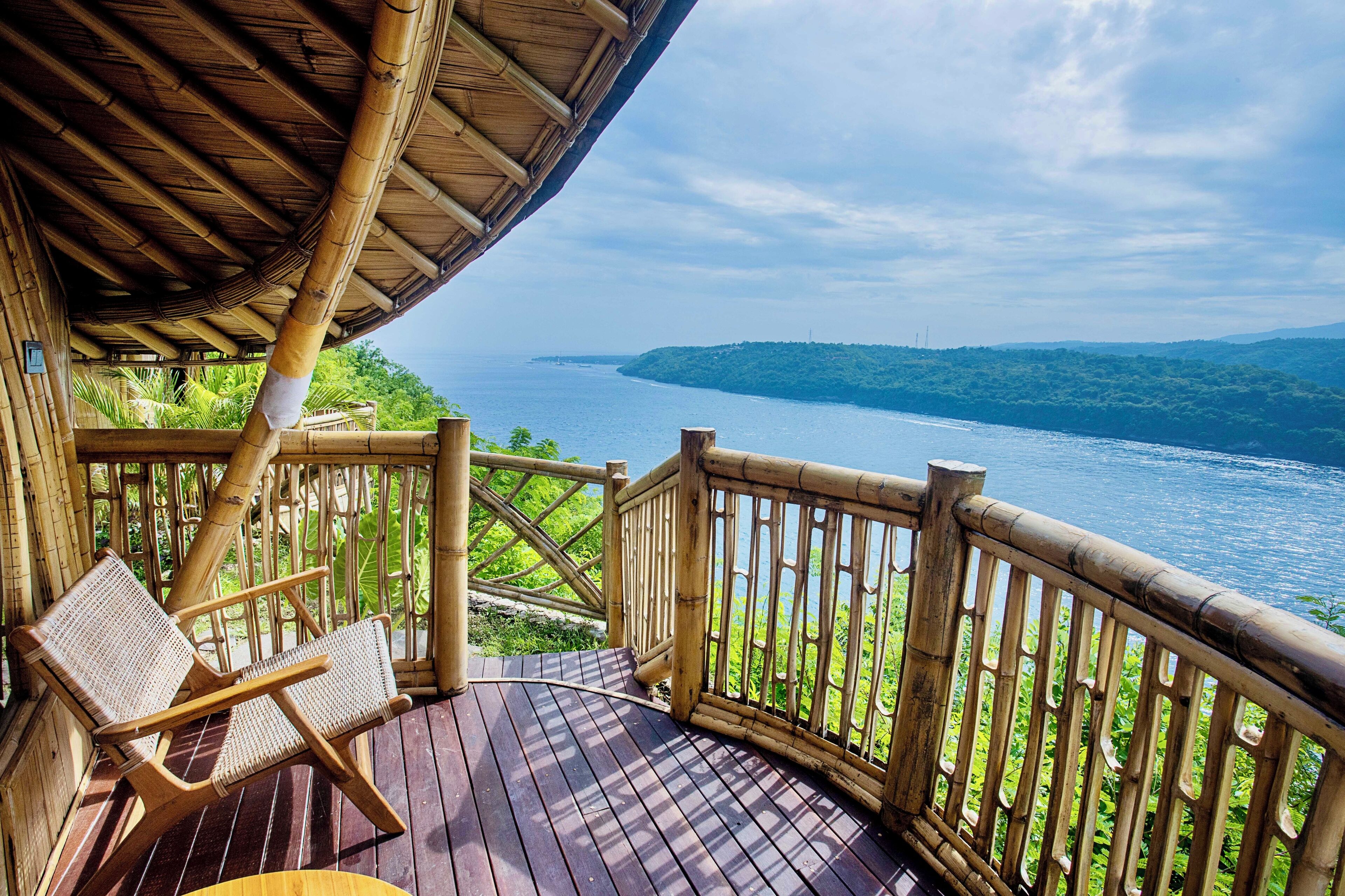 Une terrasse en bois avec deux fauteuils en osier, donnant sur une étendue d’eau et une terre lointaine.