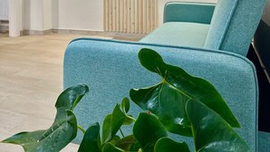 Una sala de estar moderna con un televisor de pantalla plana montado en una pared de paneles de madera, un sofá color esmeralda y una planta verde grande en primer plano.