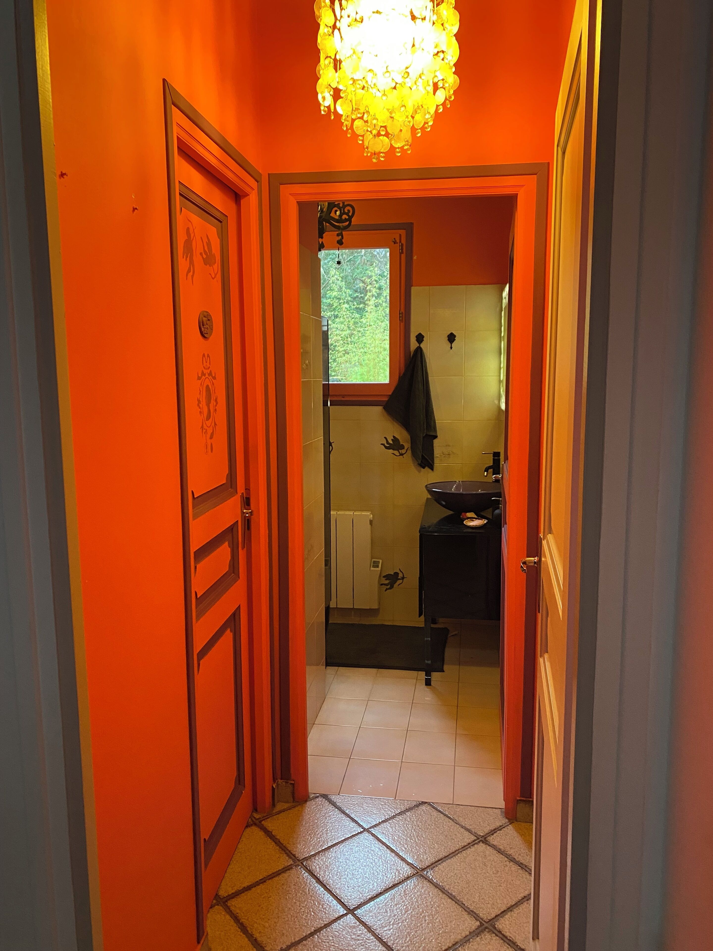 A narrow hallway with orange walls, a tiled floor, and a window with a view of greenery.