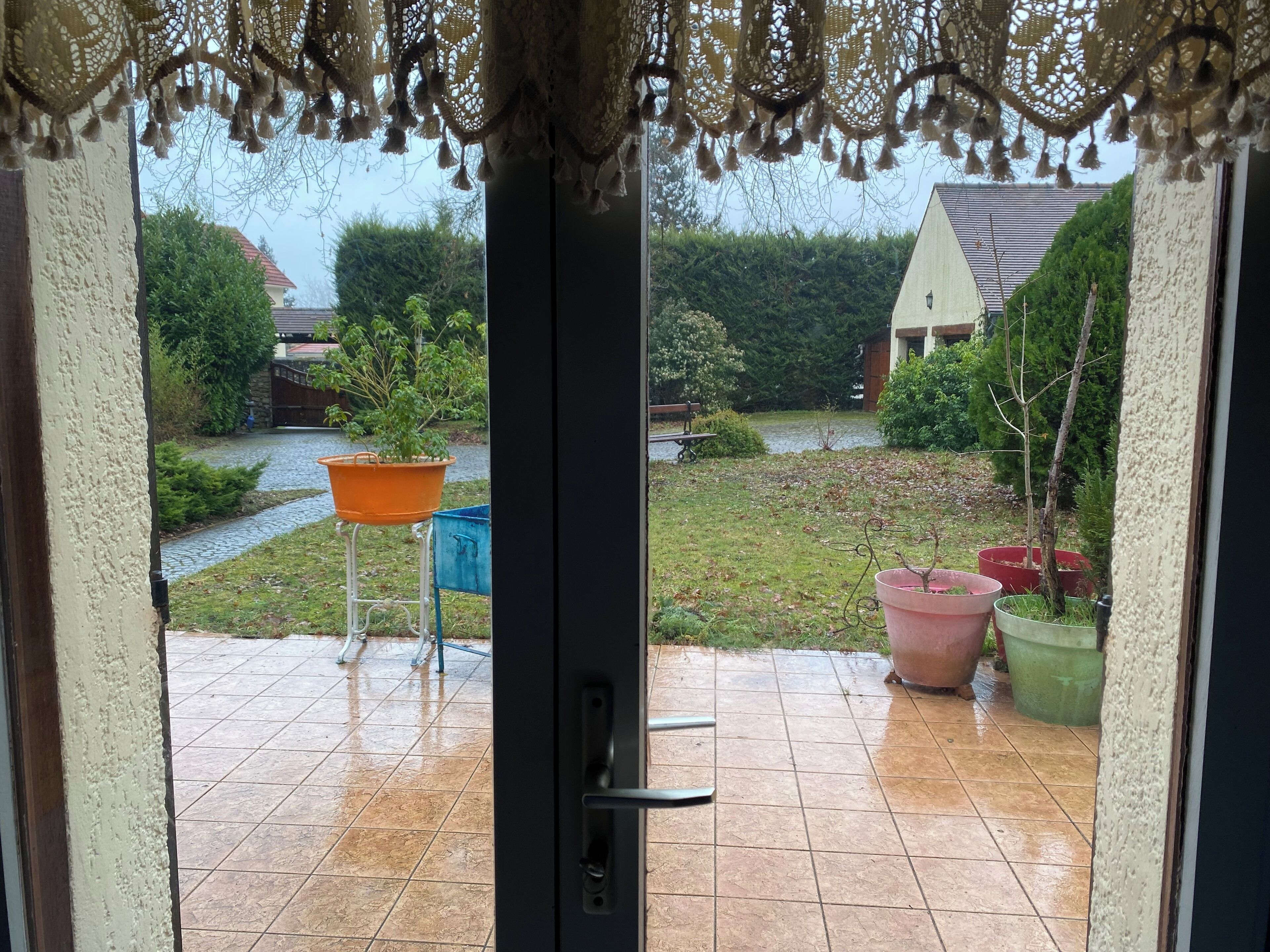 Blick von einer Tür auf eine Terrasse mit gefliestem Boden, einem kleinen Tisch und Blumentöpfen.