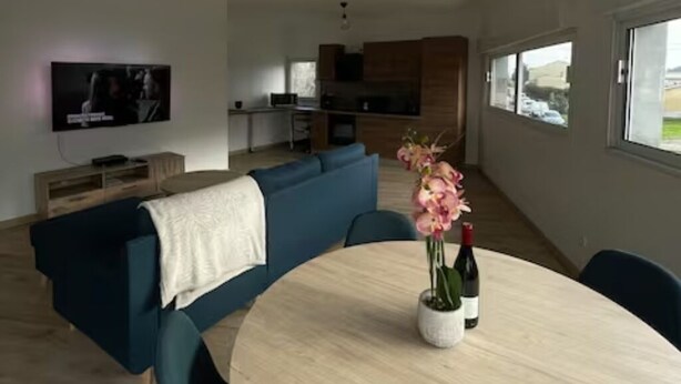 A modern living room with a round dining table, a blue sofa, and a TV mounted on the wall. - Atypical town house (Saint-Mariens)