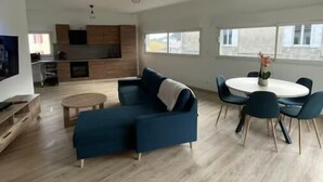 A modern living room with a sectional sofa, a dining table with chairs, and a kitchen area with wooden cabinets and a TV. - Atypical town house (Saint-Mariens)