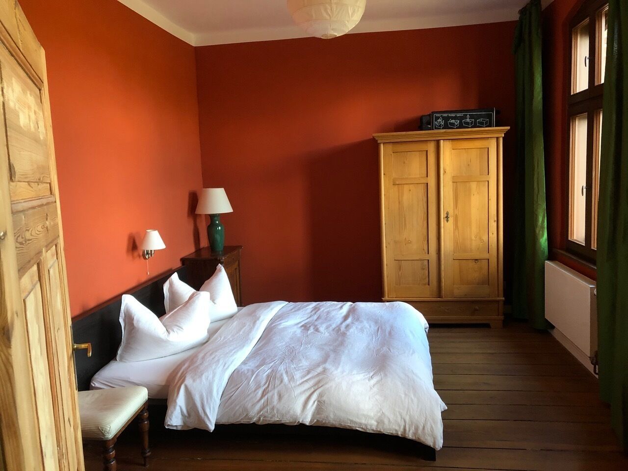 A bedroom with a large bed, wooden wardrobe, and a lamp on a nightstand.
