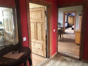 Uma porta de madeira dá acesso a um quarto com parede vermelha e piso de madeira.