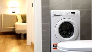 Uma lavanderia moderna com máquina de lavar frontal, sofá e luminária na parede.