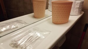 A bathroom counter with two beige paper cups, a plastic bag of cotton swabs, and a roll of toilet paper. - Loggia (Agia Galini)