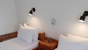 A double room with two single beds, each with white linens and pillows. There are two bedside tables, one with a lamp and the other with a small decorative item. A brown mat is placed on the floor between the beds. - Loggia (Agia Galini)