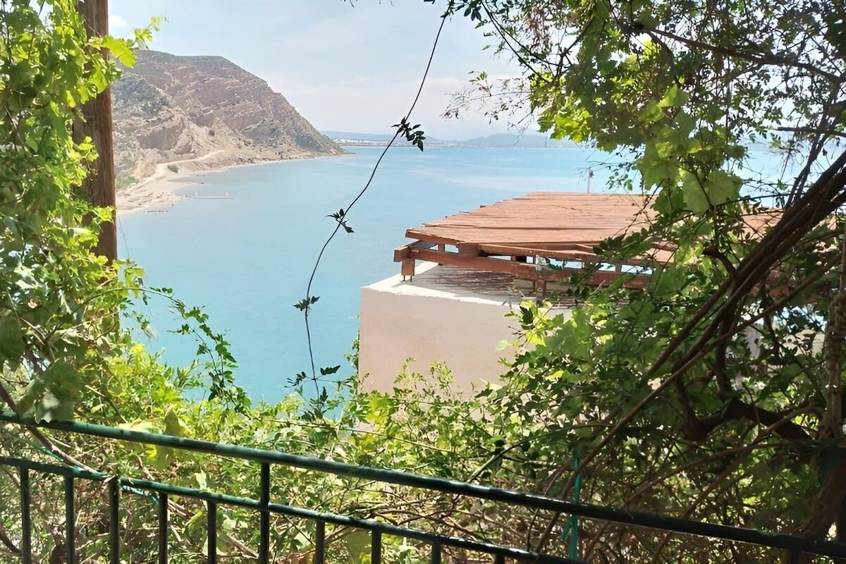 A view from a balcony overlooking a coastal area with a mountain in the background and a building with a red roof.