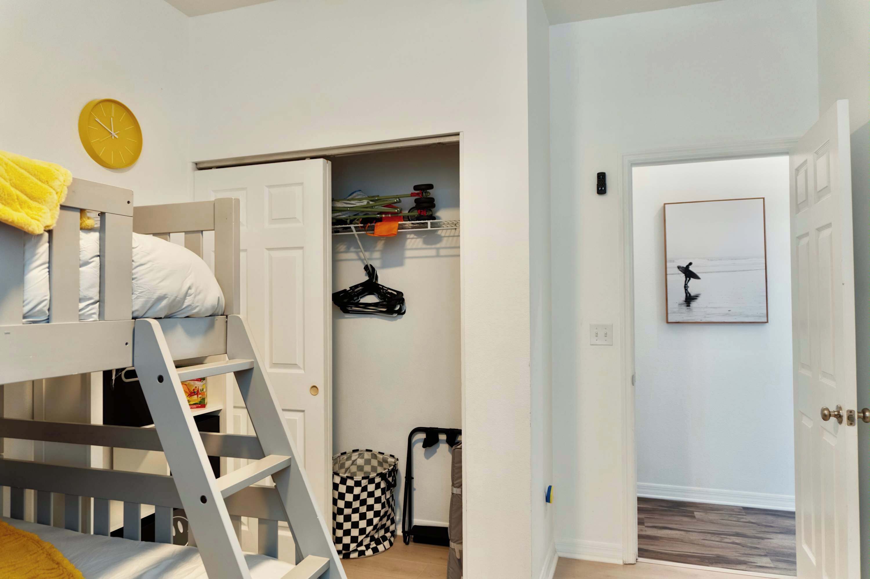 Une chambre avec un lit superposé, une petite armoire avec des étagères, une horloge et un tableau encadré au mur.