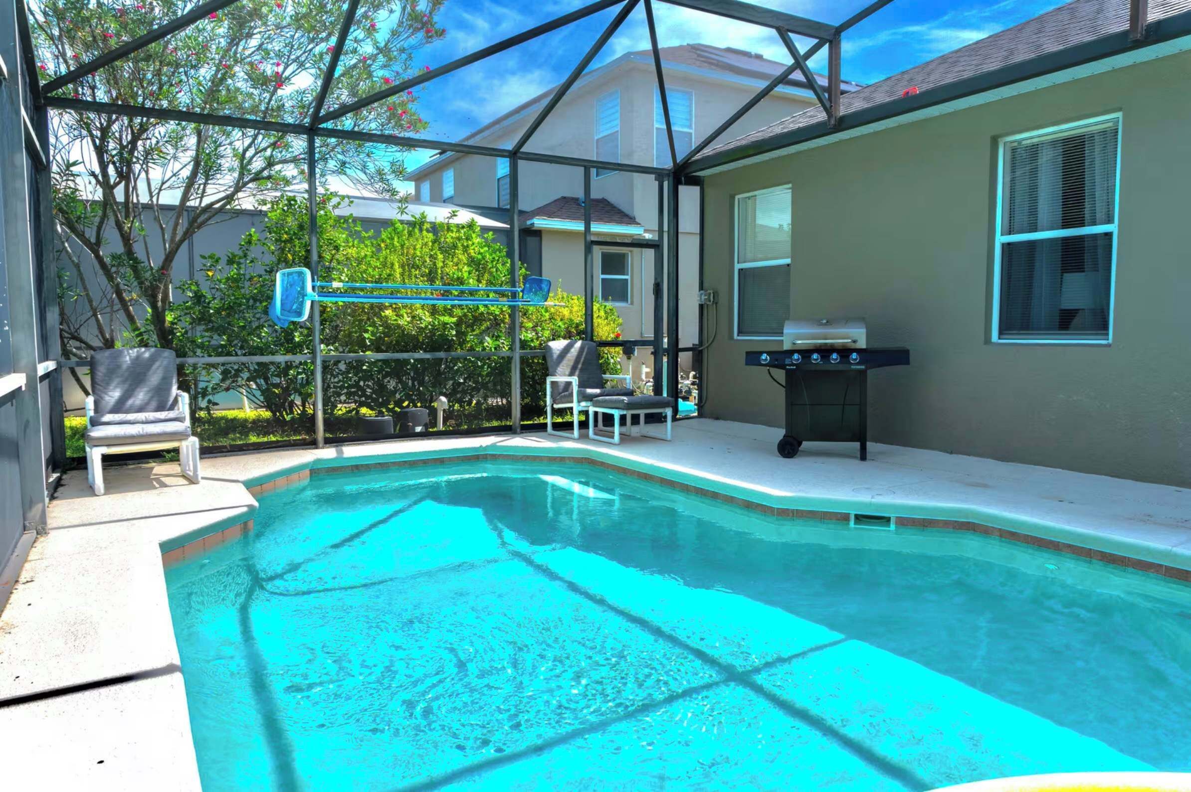 Une piscine entourée de parois en verre, un barbecue et une chaise.
