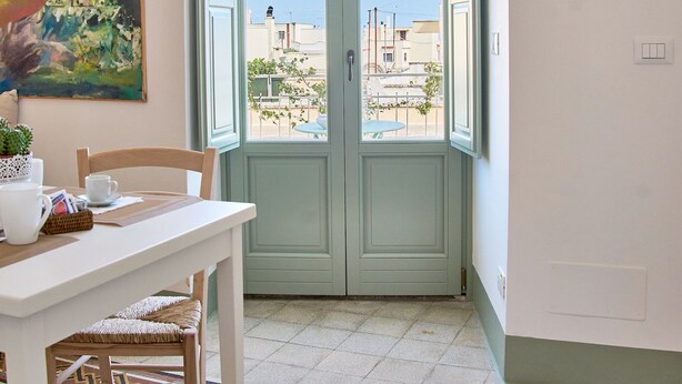 Une pièce comprenant une table à manger, des chaises, un sol à motifs, un tableau et une porte donnant sur un espace extérieur.