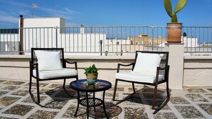 Une terrasse sur le toit avec deux chaises, une petite table et un pot de fleurs.