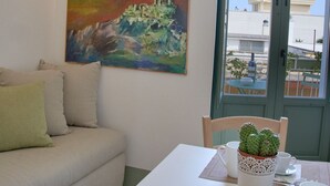 Une pièce avec un canapé blanc, une table sur laquelle est posée une plante en pot, un tableau et une vue à travers une porte.