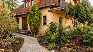 Une maison à deux étages avec une allée pavée, un balcon en bois et un jardin bien entretenu.
