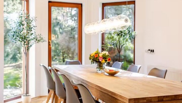 Un espace repas moderne avec une table en bois, des chaises grises et un luminaire suspendu.