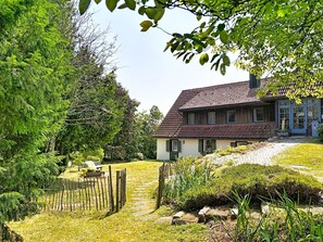 Une maison avec un toit en pente, une cour clôturée et un chemin menant à l’entrée.