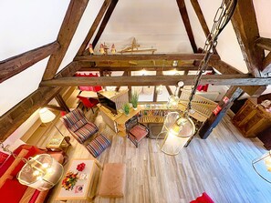 A loft-style room with exposed wooden beams, a wooden table, a red sofa, a striped armchair, and a hanging light fixture. - Schwarzwaldhof mit Pool & Sauna by Interhome (Görwihl)