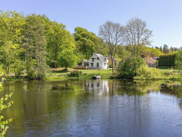 Una casa junto a un lago con un muelle, rodeada de árboles y césped.