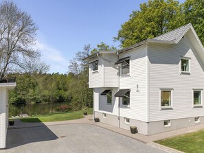 Un edificio blanco de dos pisos con el número 211, un camino de entrada y un estanque al fondo.