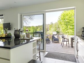 A modern kitchen with a large window, a dining area with chairs, and a view of a lake and trees. - Villa Anja by Interhome (Asarum)
