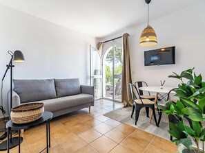 Ein modernes Wohnzimmer mit einem grauen Sofa, einem Esstisch mit Stühlen, einem an der Wand befestigten Fernseher und einem großen Fenster mit Vorhängen.