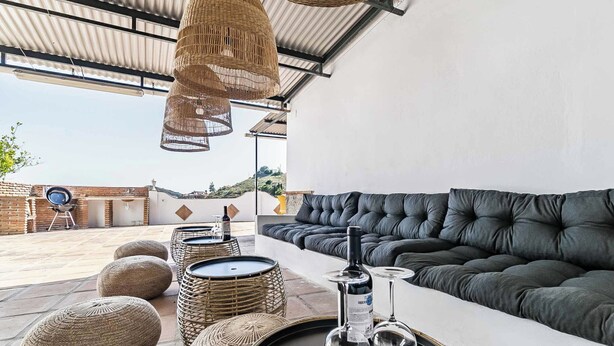 Un espace de détente extérieur moderne, avec un canapé et des tables rondes, des poufs en osier et des lampes suspendues en osier.
