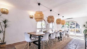 Un espace repas avec une longue table en bois, des chaises blanches et des suspensions en fibres tressées.