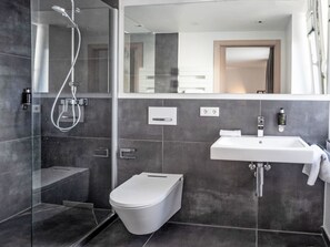 Ein modernes Badezimmer mit einer Duschkabine, einer weißen Toilette und einem großen Spiegel über dem Waschbecken.