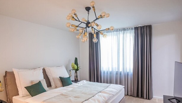 A modern bedroom with a large bed, a chandelier, a plant, and a TV. - Munich Finest Apartments Studio 1 by Interhome (Munich)