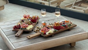 A terrace with a wooden table set for a meal, two glasses of white wine, and lounge chairs with a scenic view in the background. - Petit Coin de Paradis (Alata)