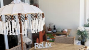 A wooden dining table with a white umbrella and a 'Relax' sign. - Petit Coin de Paradis (Alata)