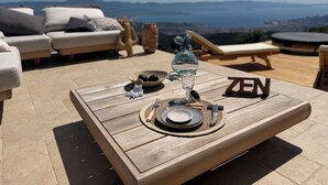 A wooden table with a glass of water, a bowl of fruit, and a plate with cutlery. The word 'ZEN' is visible on the table. - Petit Coin de Paradis (Alata)
