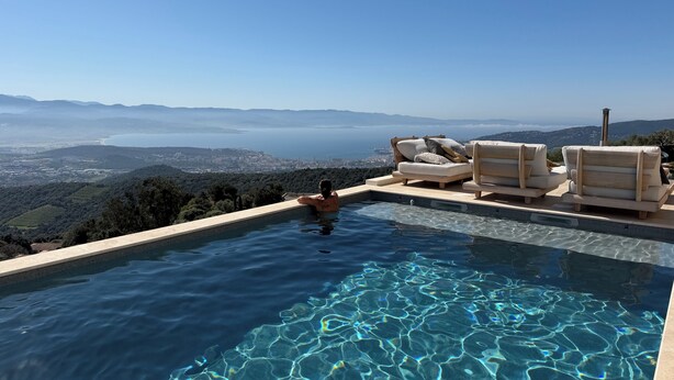 A infinity pool with clear water, a person relaxing, and a view of a coastal city. - Petit Coin de Paradis (Alata)