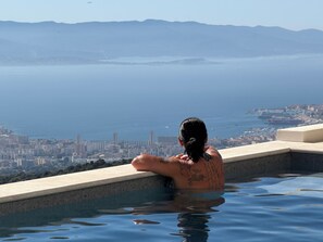 Una persona en una piscina con un paisaje urbano y montañas al fondo.