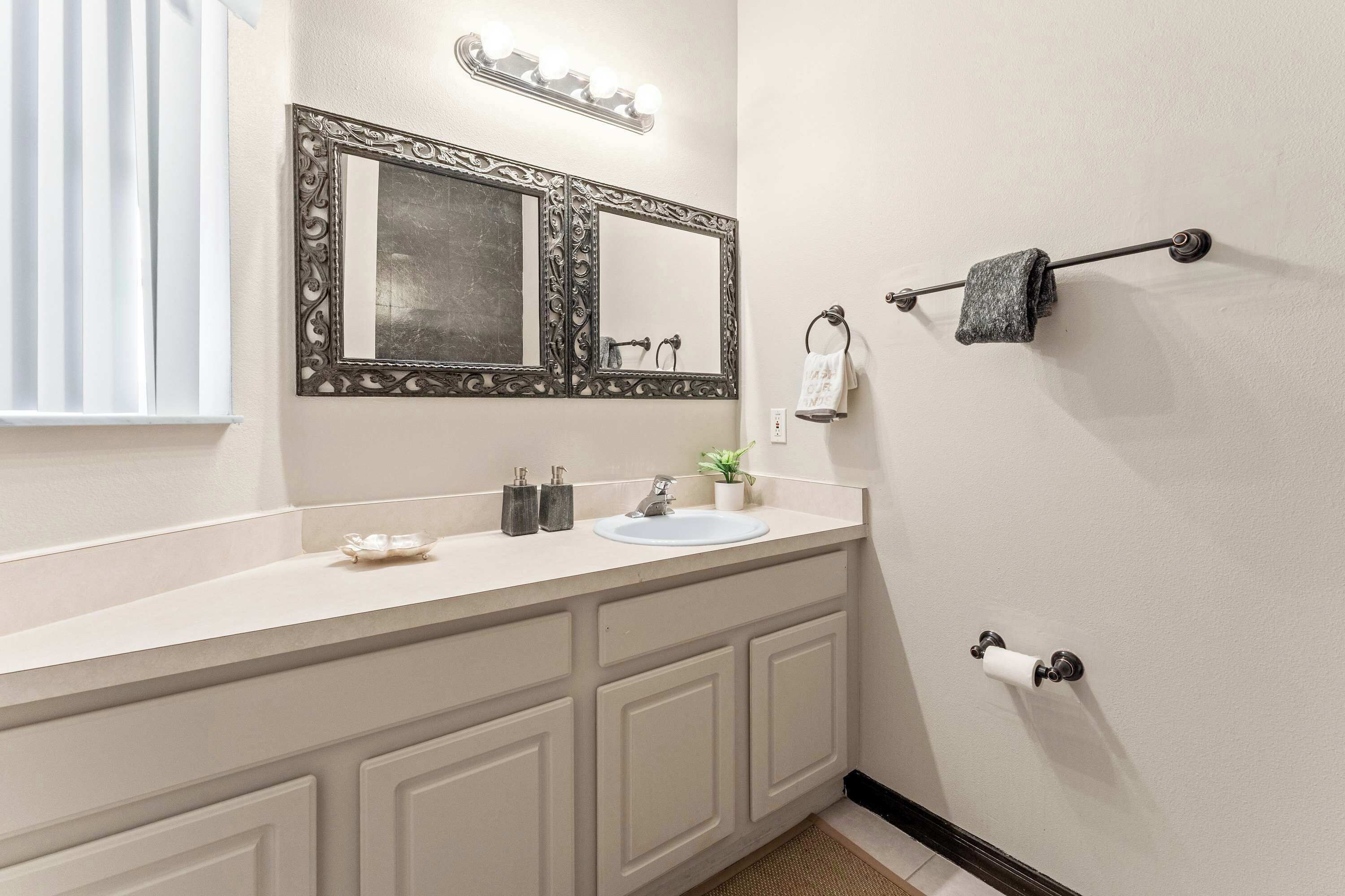 Un baño con lavamanos doble, un espejo grande, un perchero para toallas y un dispensador de papel higiénico.
